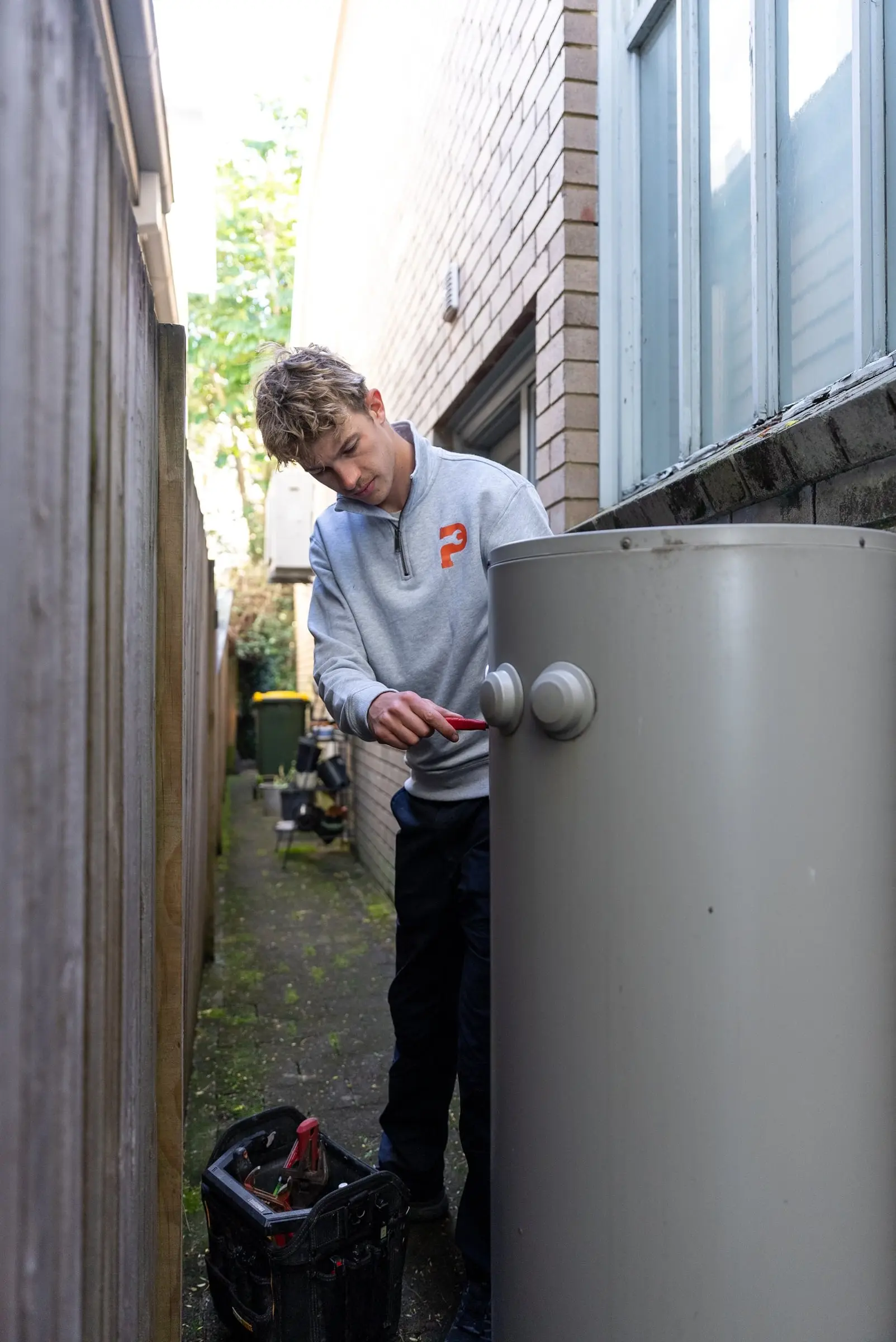 Plumber working on a hot water storage tank in a side passage