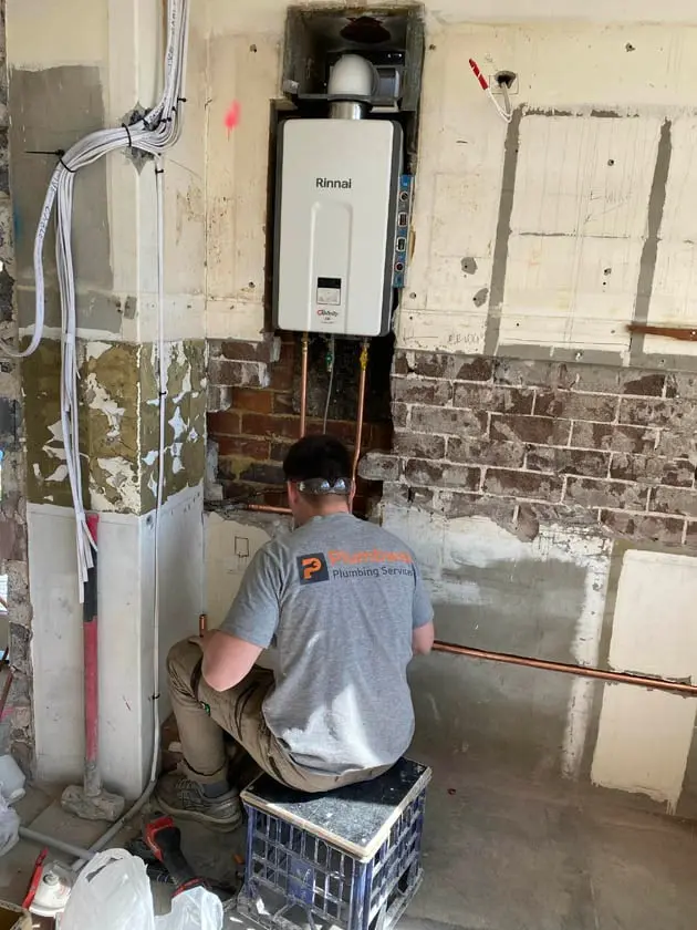 Plumber installing a continuous flow hot water unit on a renovation wall