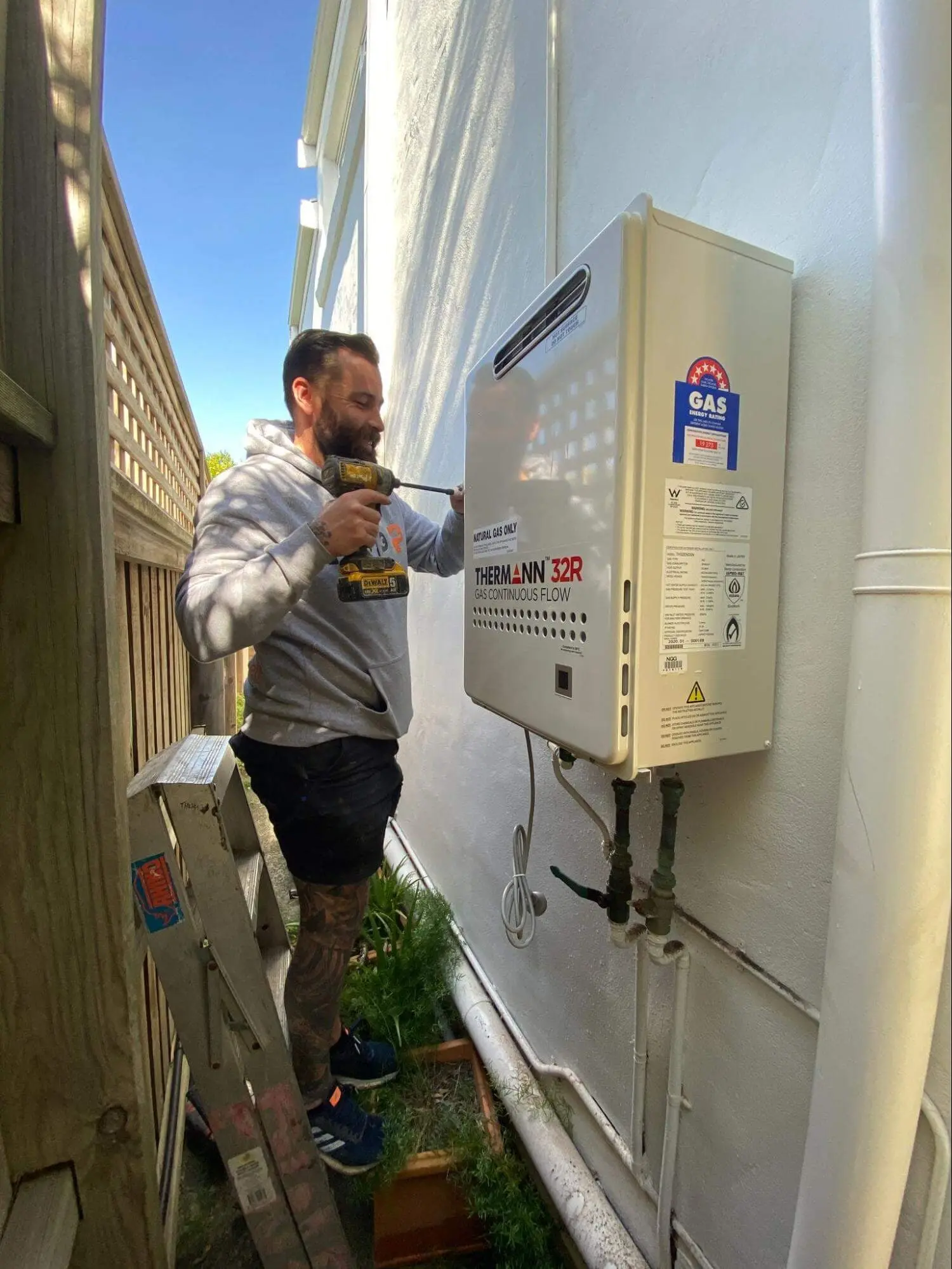 Plumber installing a continuous flow hot water unit in a side passage