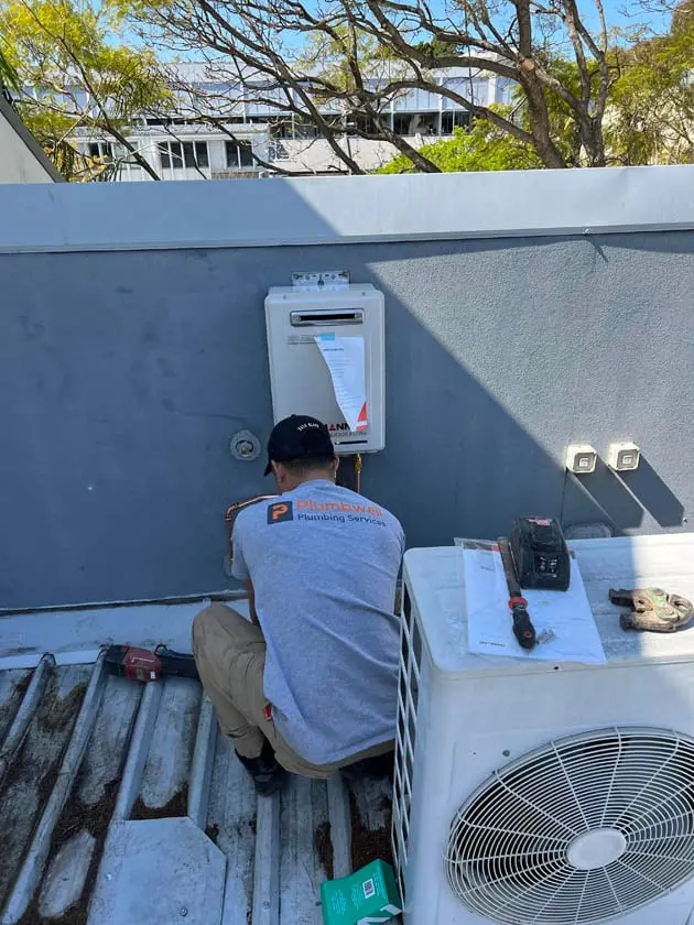 Plumber installing a hot water unit on a flat roof