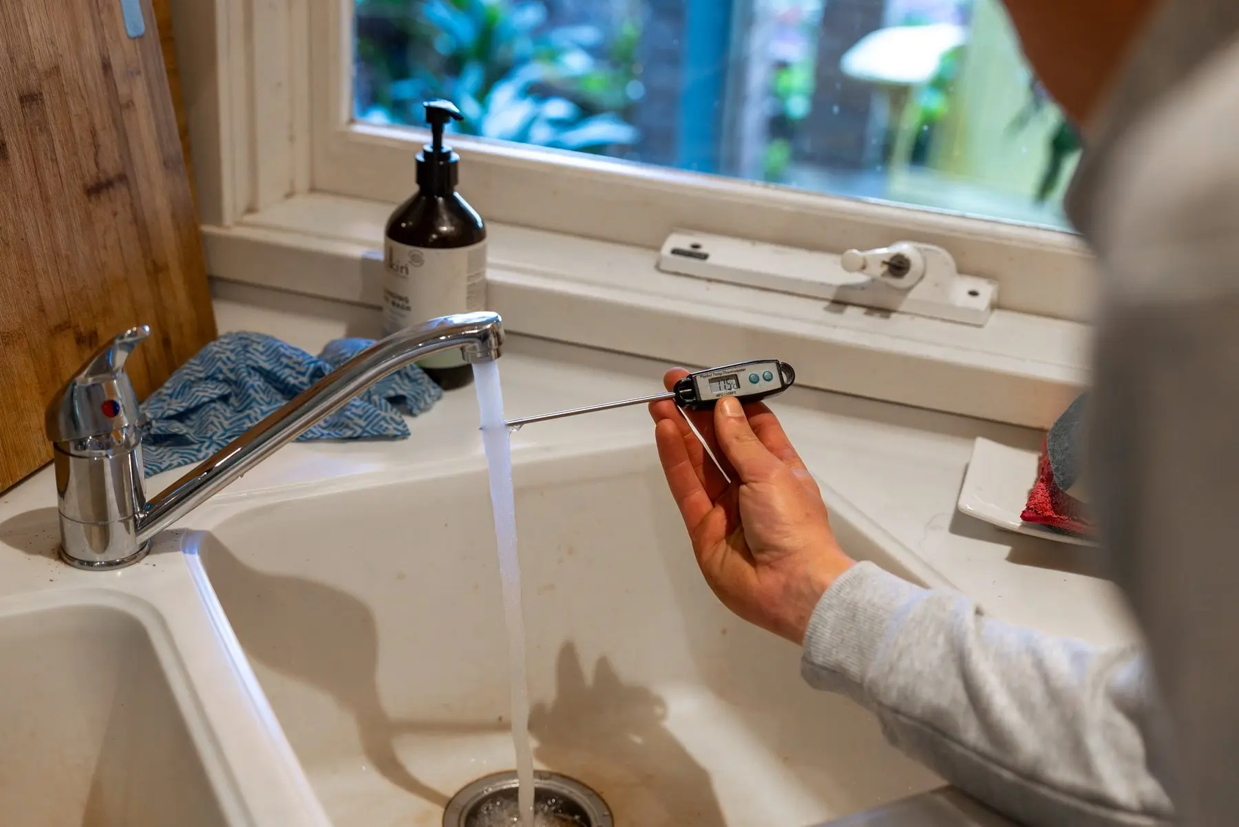 Thermometer checking the water temperature at a running kitchen tap
